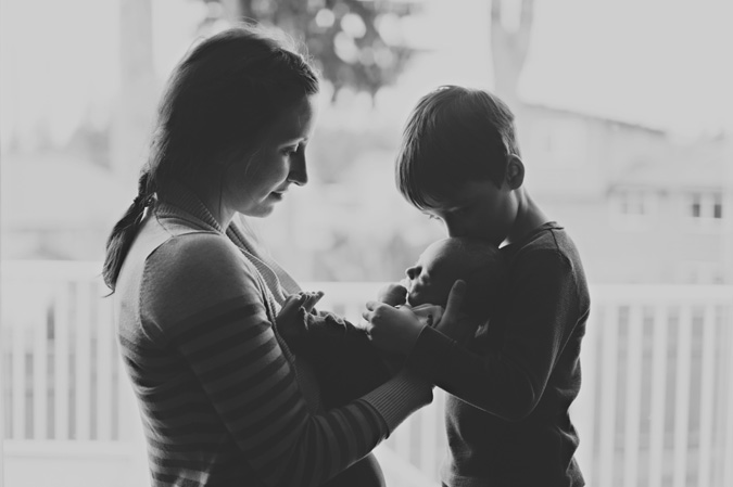 a little boy kissing his newborn baby brother cradled in his mother's arms, cambell river bc